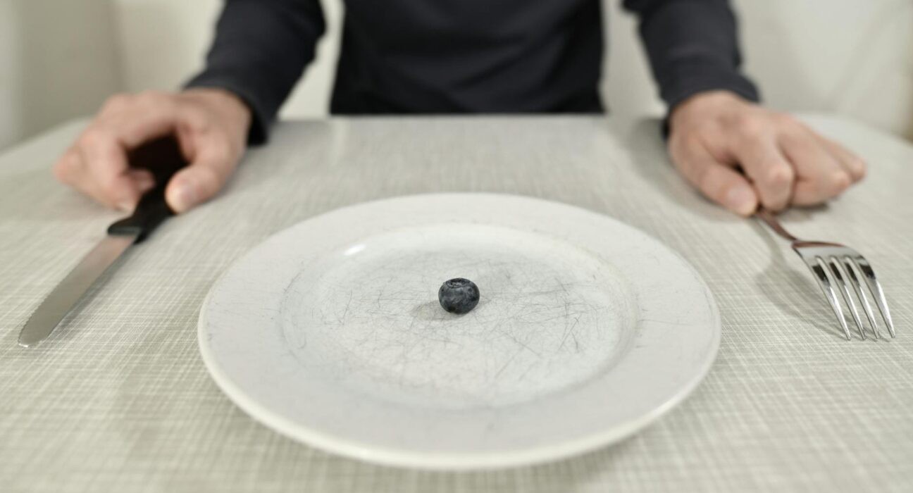 A single blueberry on a scratched plate symbolizes minimalist diet and portion control.