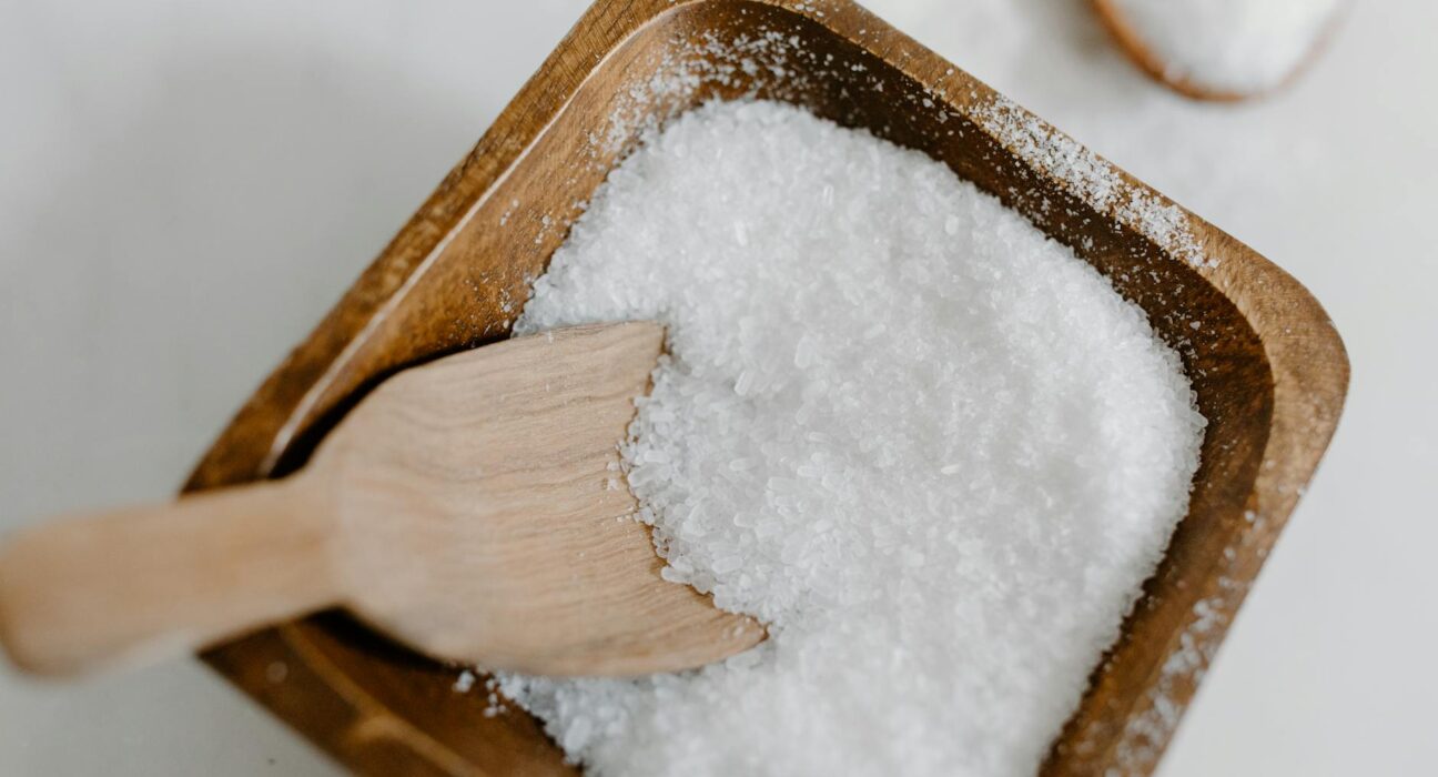 Close-up of coarse sea salt in a wooden bowl with a wooden scoop, perfect for culinary use.