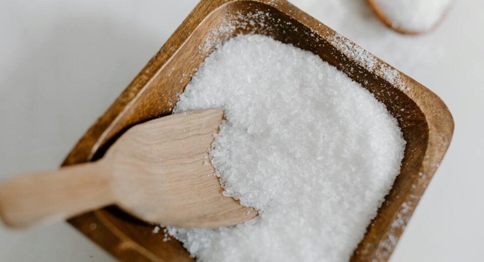 Close-up of coarse sea salt in a wooden bowl with a wooden scoop, perfect for culinary use.