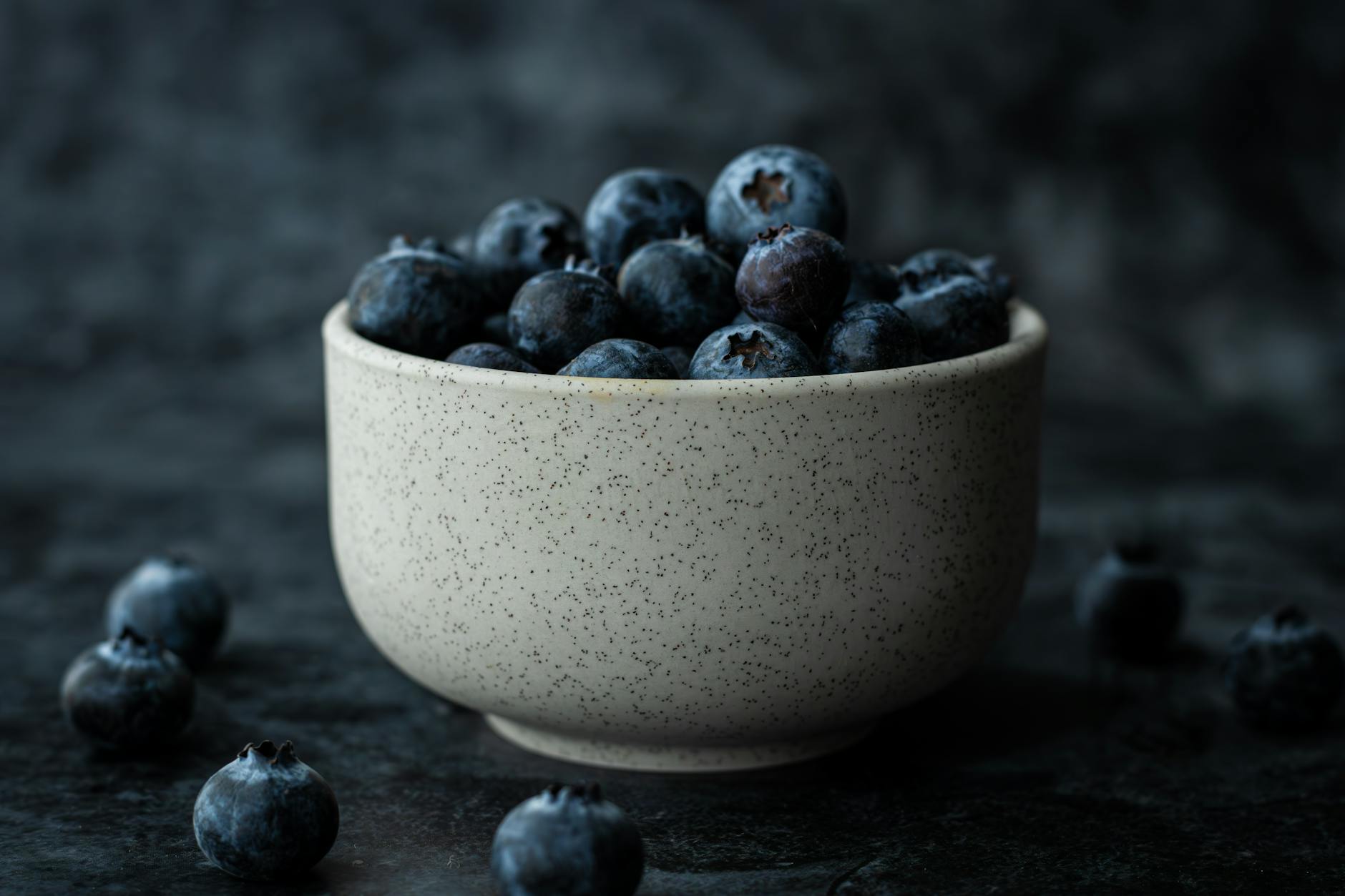 A bowl of ripe blueberries against a dark backdrop, highlighting their freshness and rich color.