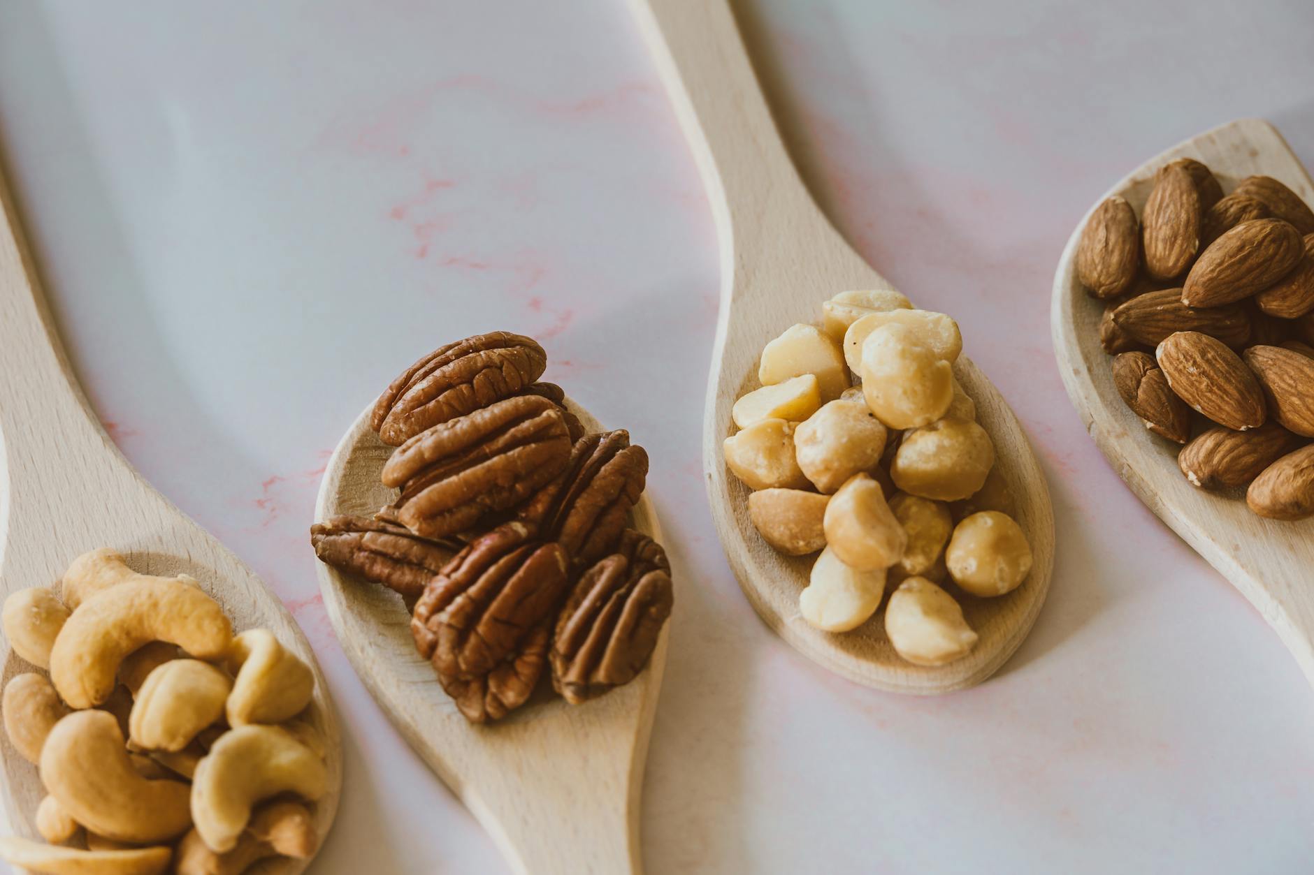 Close-up of assorted nuts like almonds, pecans, cashews, and macadamia on wooden spoons.