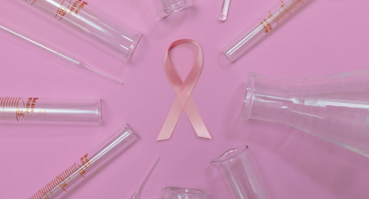 A pink ribbon surrounded by laboratory glassware symbolizes breast cancer research and awareness.