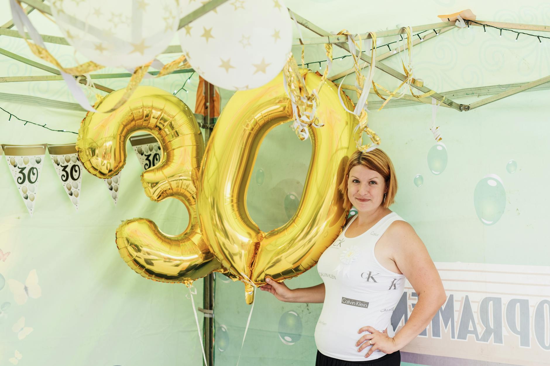 Woman posing with golden number 30 balloons at a birthday party celebration.