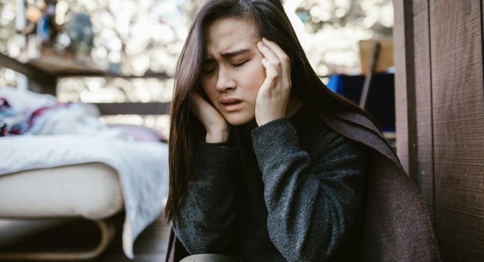 A young woman holds her head in distress while sitting indoors, capturing an emotional moment.