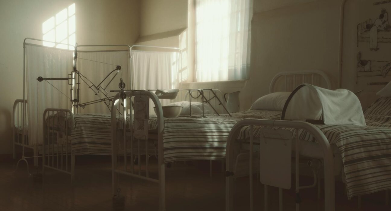 Dimly lit vintage hospital room featuring empty beds and medical equipment, creating a nostalgic atmosphere.