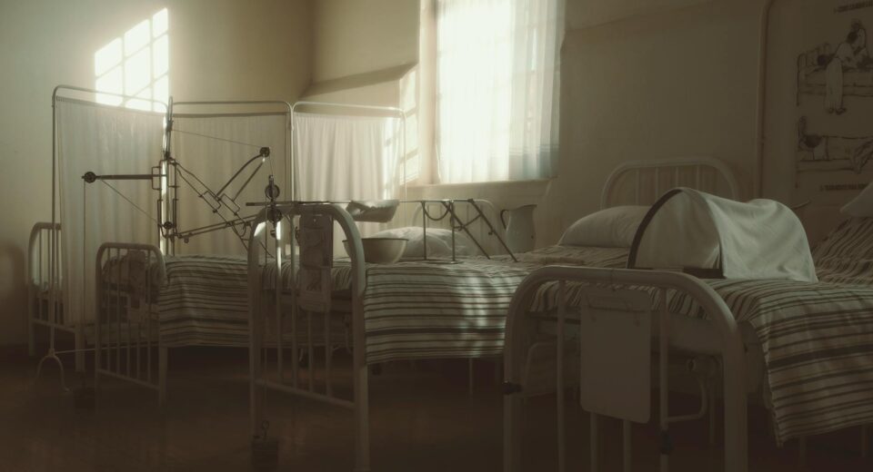 Dimly lit vintage hospital room featuring empty beds and medical equipment, creating a nostalgic atmosphere.