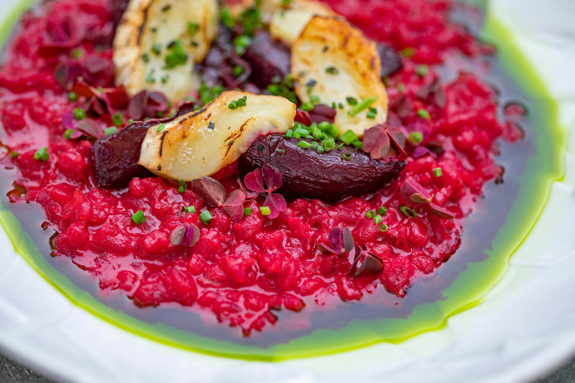 A colorful beetroot risotto topped with grilled halloumi and fresh herbs on a white plate.