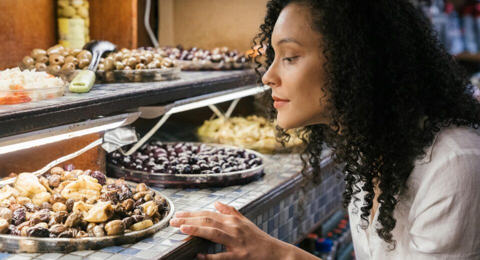 A woman observes a display filled with a variety of olives and other foods.