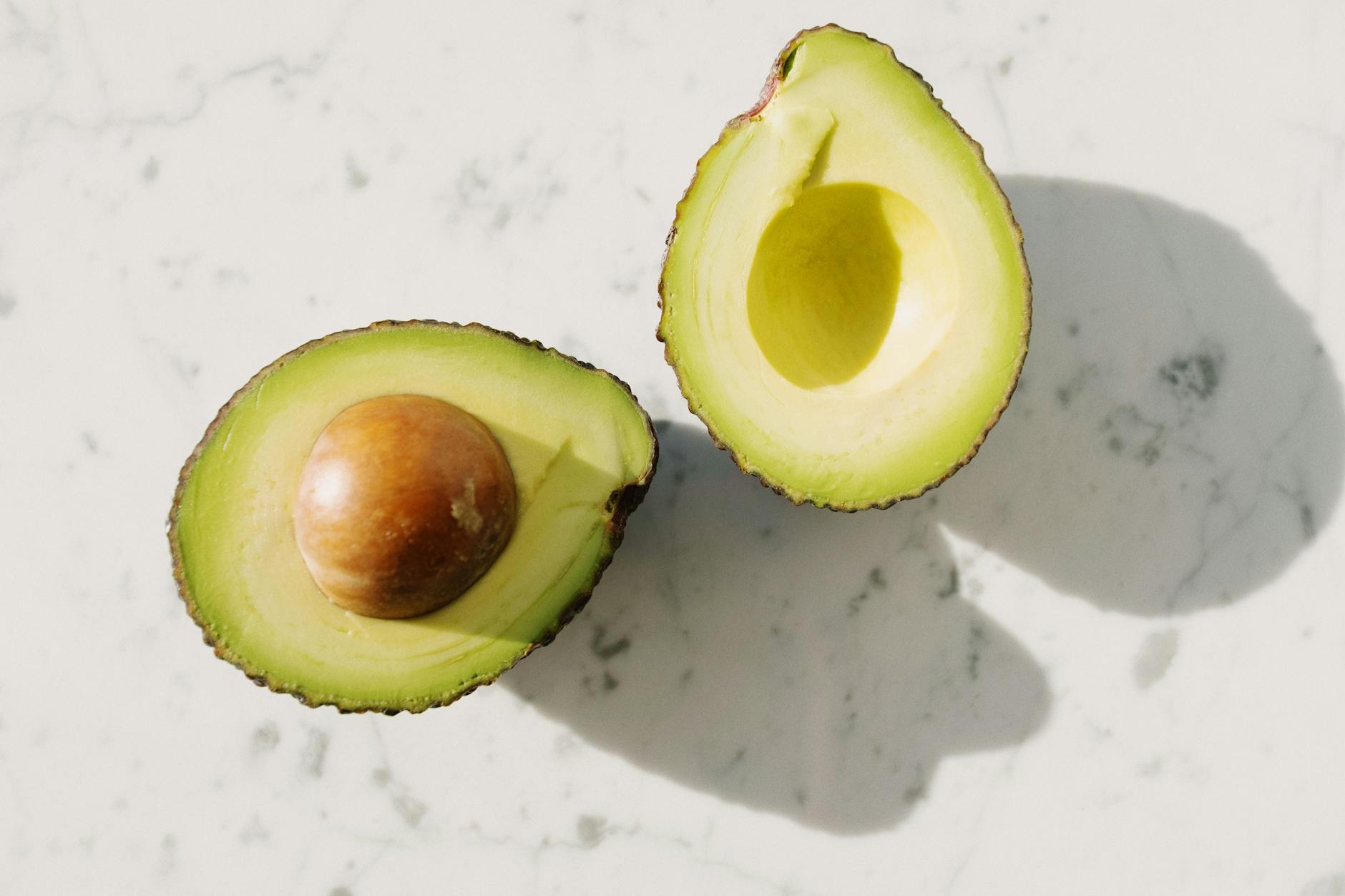 Close-up of two fresh avocado halves on a marble surface, displaying vibrant green color and seed.