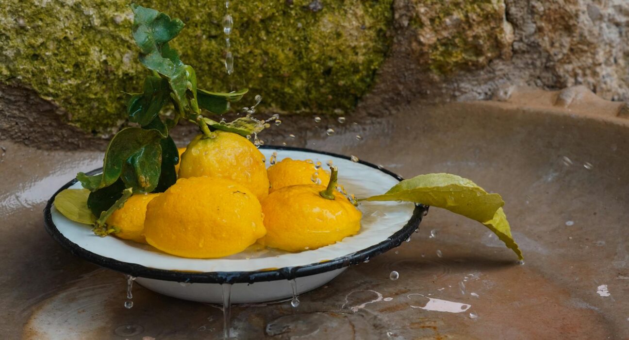 Vibrant yellow lemons in an enamel bowl with water droplets, against a rustic background.