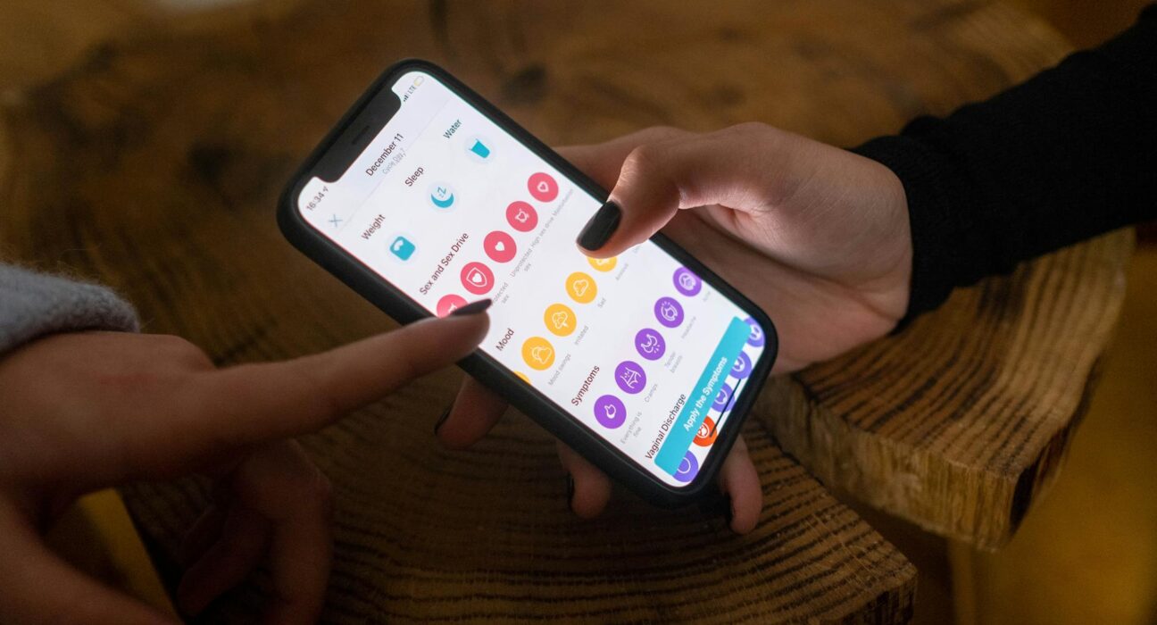 Close-up of hands using a fertility tracking app on a smartphone indoors.