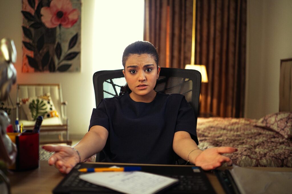 A woman looking confused while working from home at a desk in her bedroom.