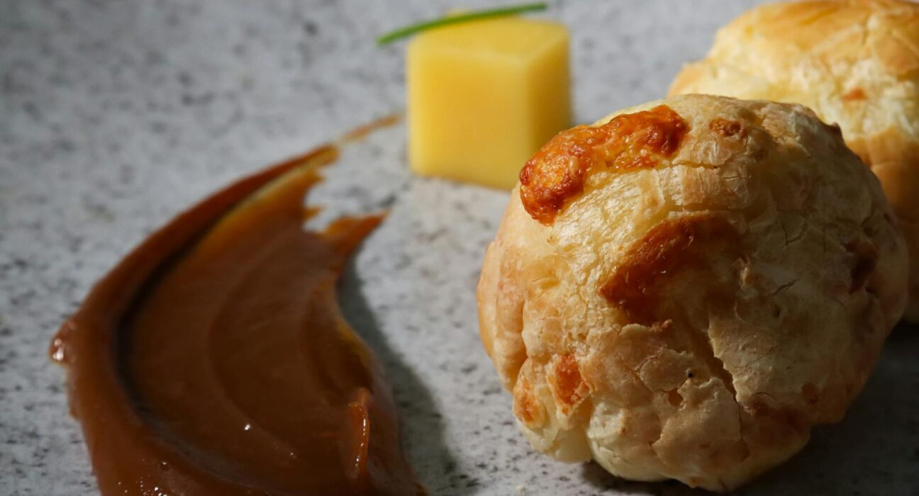 Savory cheese pastries garnished with sauce and cheese cube on marble surface, ideal for gourmet food themes.