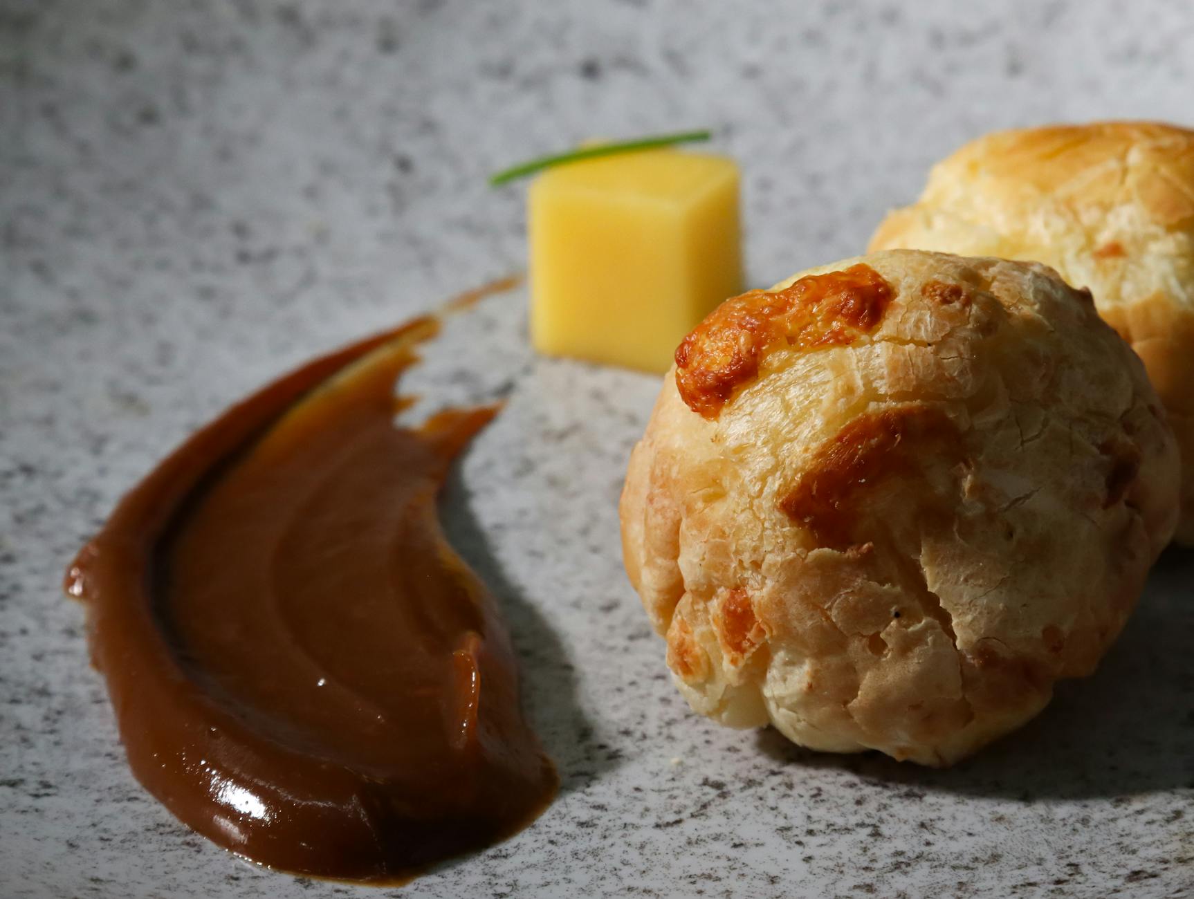 Savory cheese pastries garnished with sauce and cheese cube on marble surface, ideal for gourmet food themes.