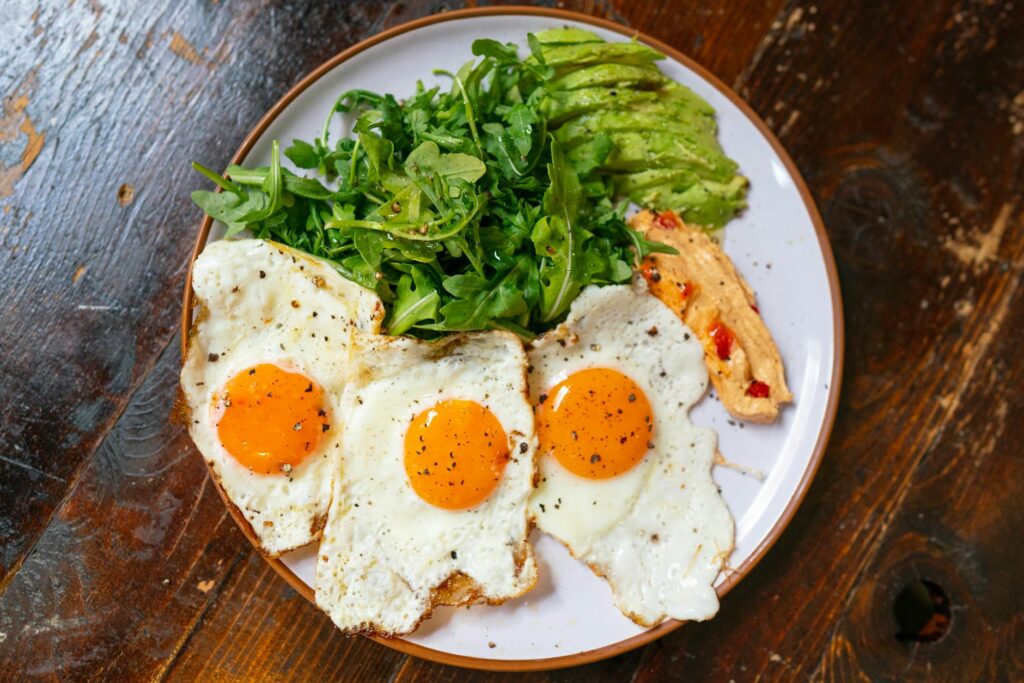 Top view of a breakfast plate with eggs, arugula, avocado, and spread.