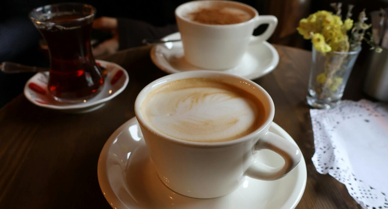 Inviting scene with two lattes and a tea glass on a wooden table, perfect for coffee shop vibes.