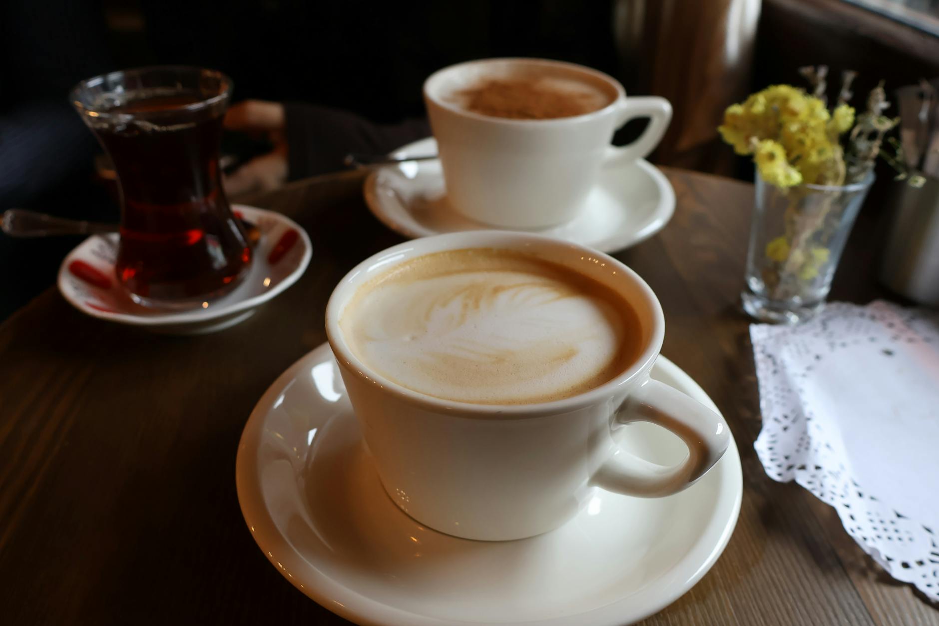 Inviting scene with two lattes and a tea glass on a wooden table, perfect for coffee shop vibes.