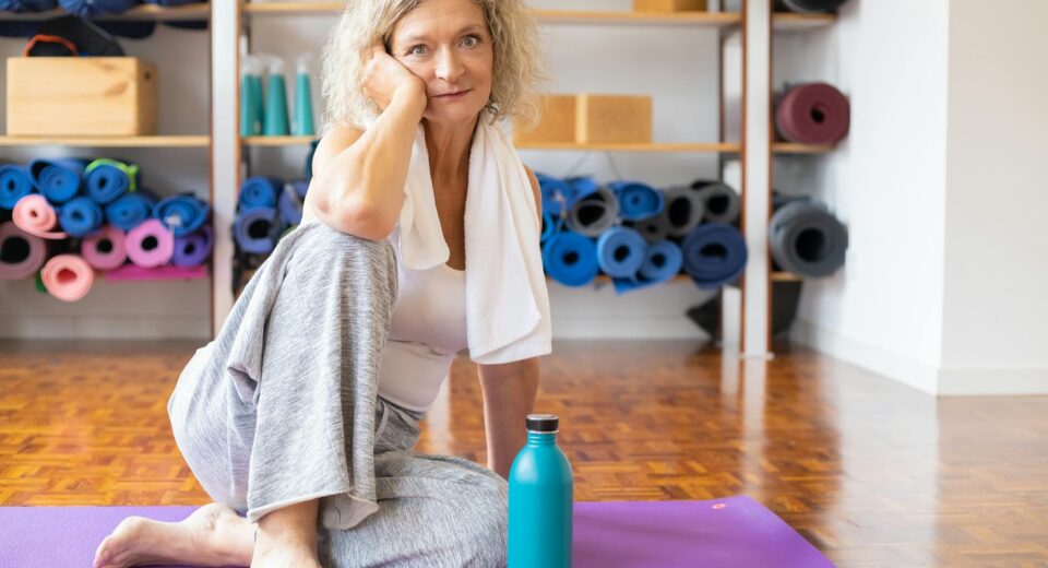 Senior woman resting on a yoga mat in a modern studio with equipment in the background.