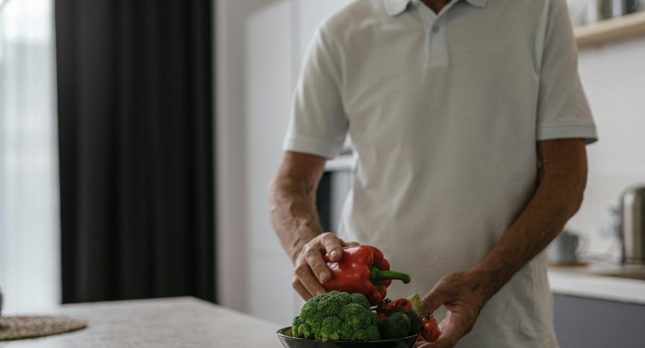 Elderly man in kitchen holding vegetables, embracing a healthy lifestyle.