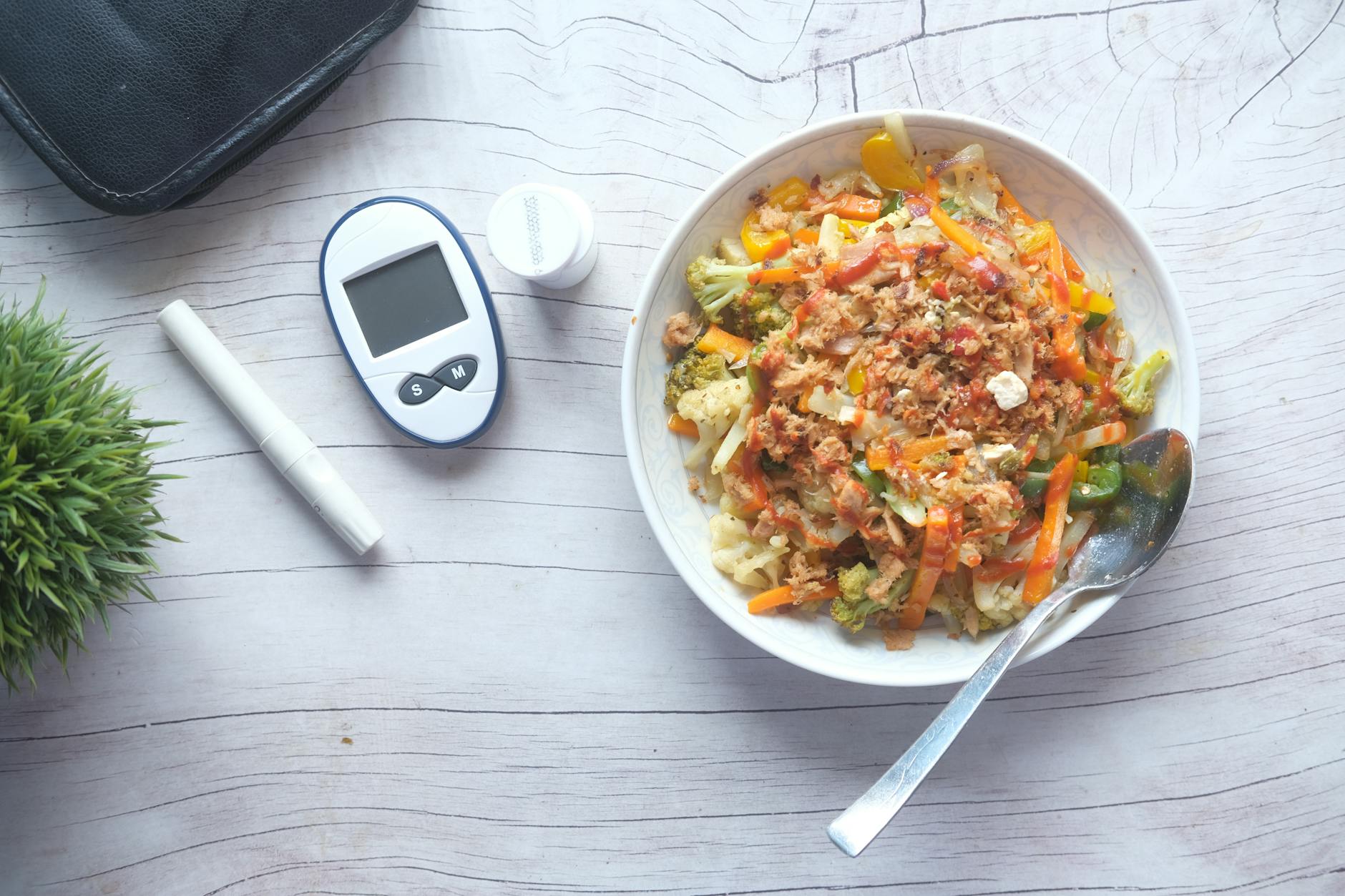 Top view of a nutritious vegetable salad next to diabetic monitoring equipment on a wooden table.