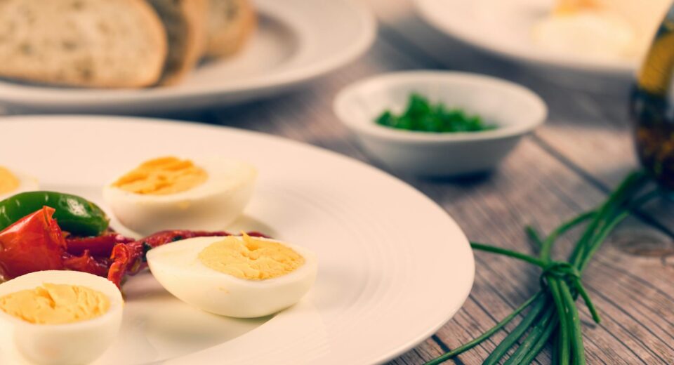 Delicious homemade sliced boiled eggs served with herbs and vegetables on a rustic wooden table.