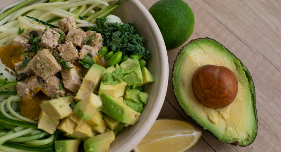 Delicious vegan bowl with zoodles, avocado, tofu, and greens on a wooden table.