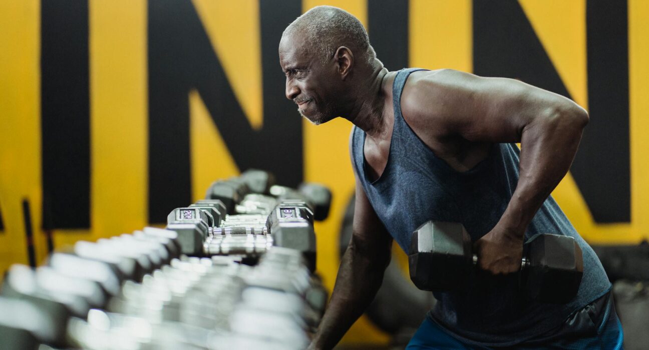 Strong senior man focusing on strength training with dumbbells in a vibrant gym.
