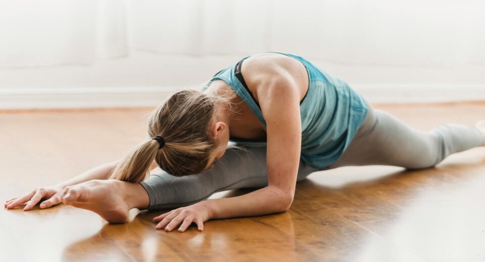 Slim active anonymous female in sportswear stretching on timber floor of home in daylight