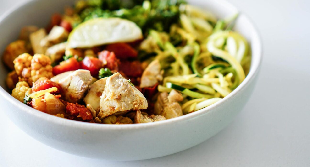 Close-up of a nutritious bowl with chicken, zucchini noodles, and vegetables.