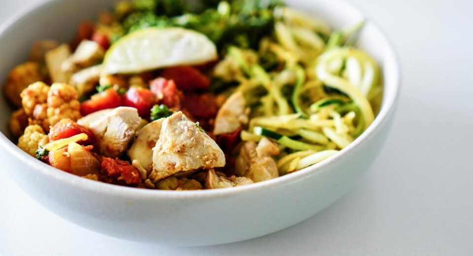 Close-up of a nutritious bowl with chicken, zucchini noodles, and vegetables.
