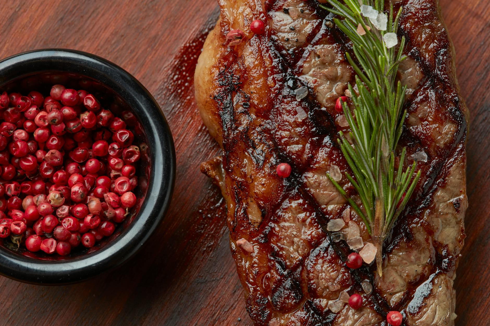 Close-up of grilled steak garnished with rosemary and pink peppercorns, enhancing its flavor.