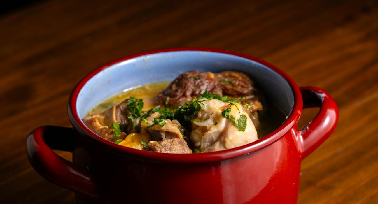 Warm and comforting hearty stew served in a rustic red pot on wood surface.