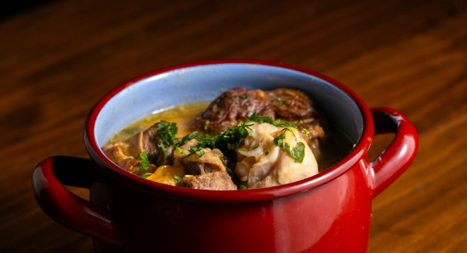 Warm and comforting hearty stew served in a rustic red pot on wood surface.