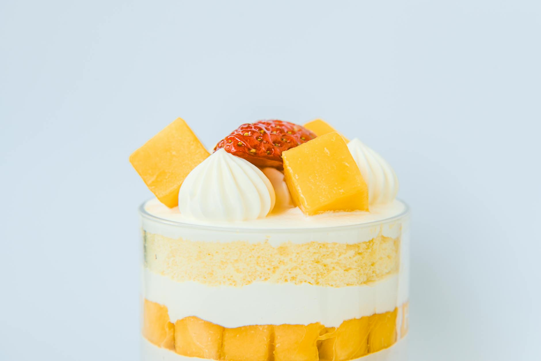 Close-up of a layered mango and strawberry trifle topped with fresh fruit and whipped cream.