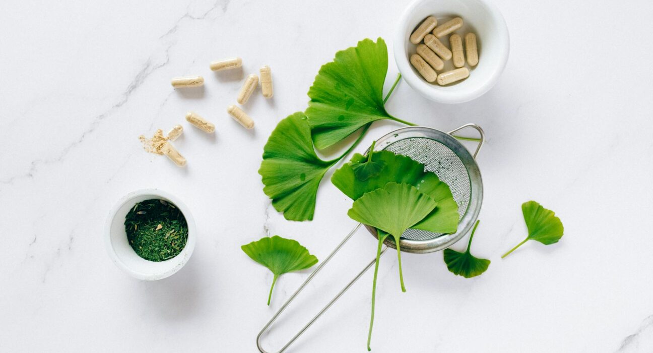 Flat lay of ginkgo leaves, capsules, and herbal powder on marble for natural health remedy.