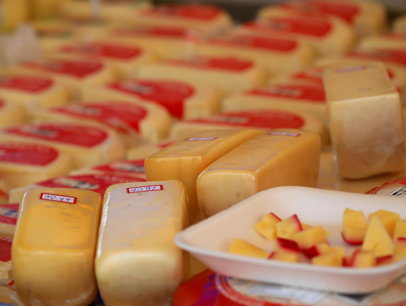 Variety of cheese blocks and samples on display at a market stall.