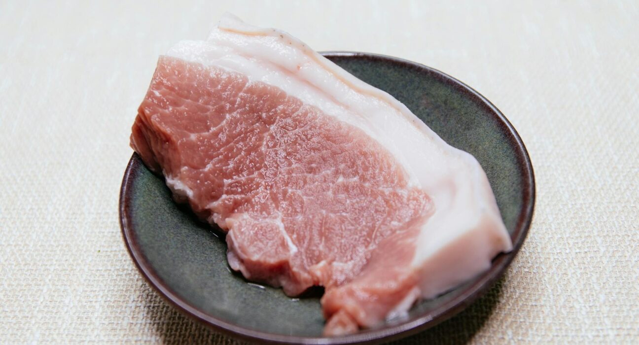 Close-up of a raw pork slice on a dark plate, ideal for culinary themes.