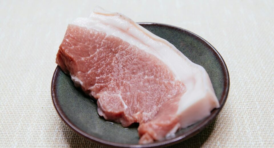 Close-up of a raw pork slice on a dark plate, ideal for culinary themes.
