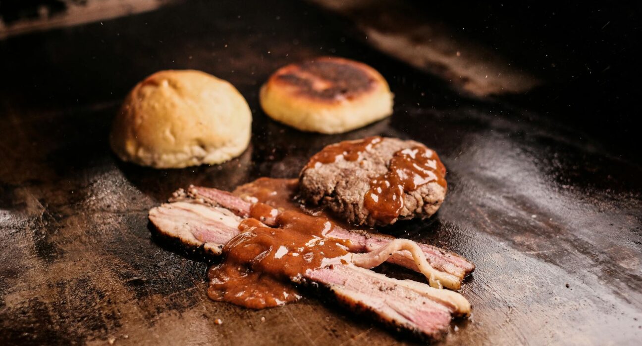 Close-up of grilled meats with savory sauce and buns, sizzling on a hot grill. Captures the essence of barbecue.