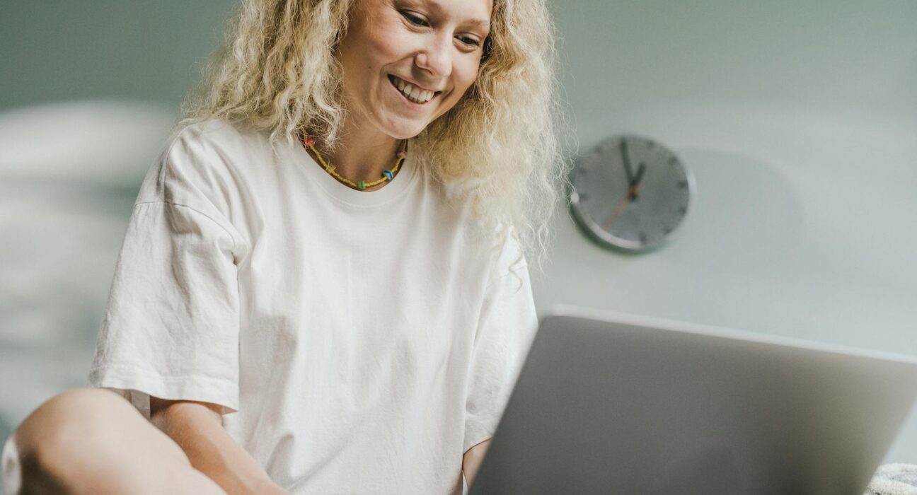 A cheerful woman with blonde hair working on a laptop indoors