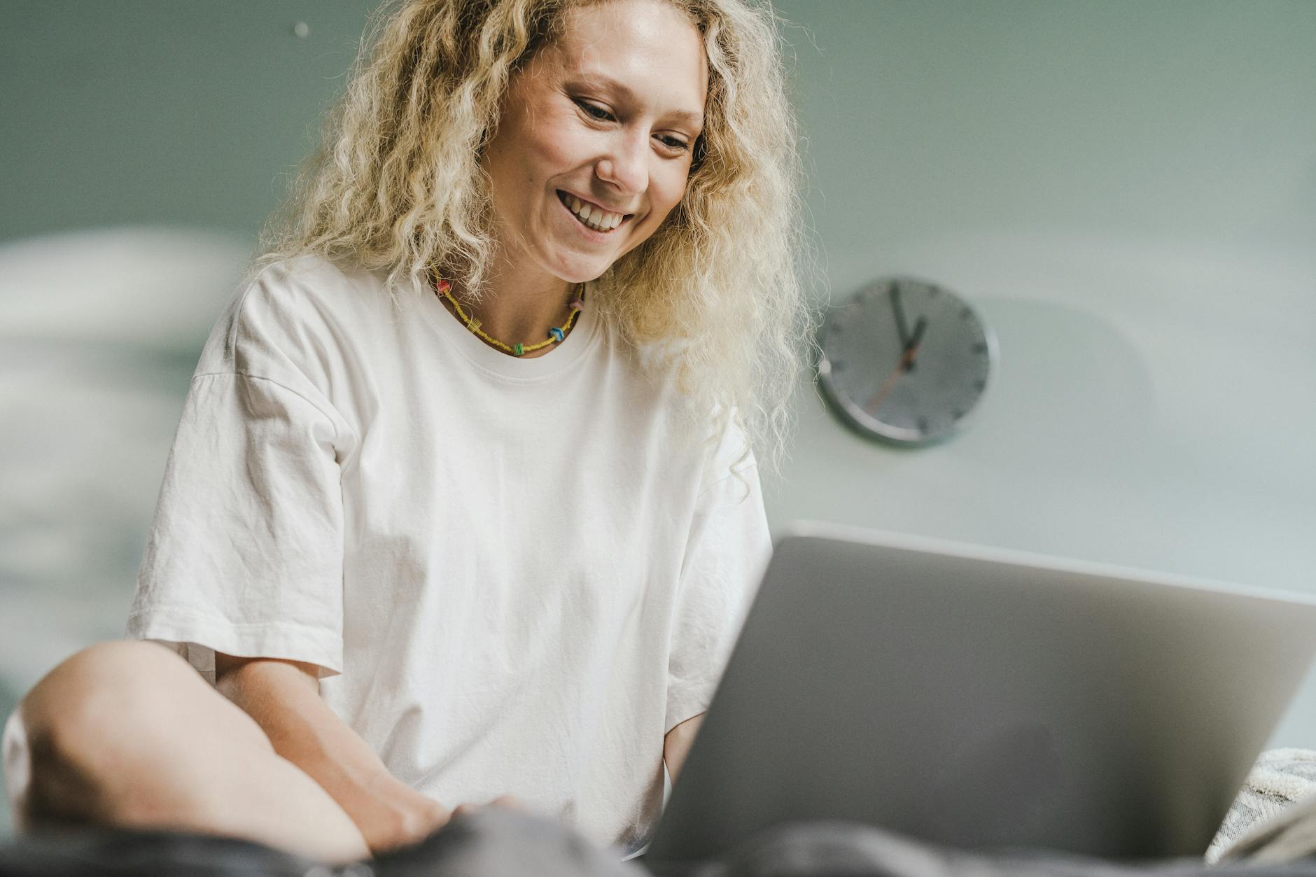 A cheerful woman with blonde hair working on a laptop indoors