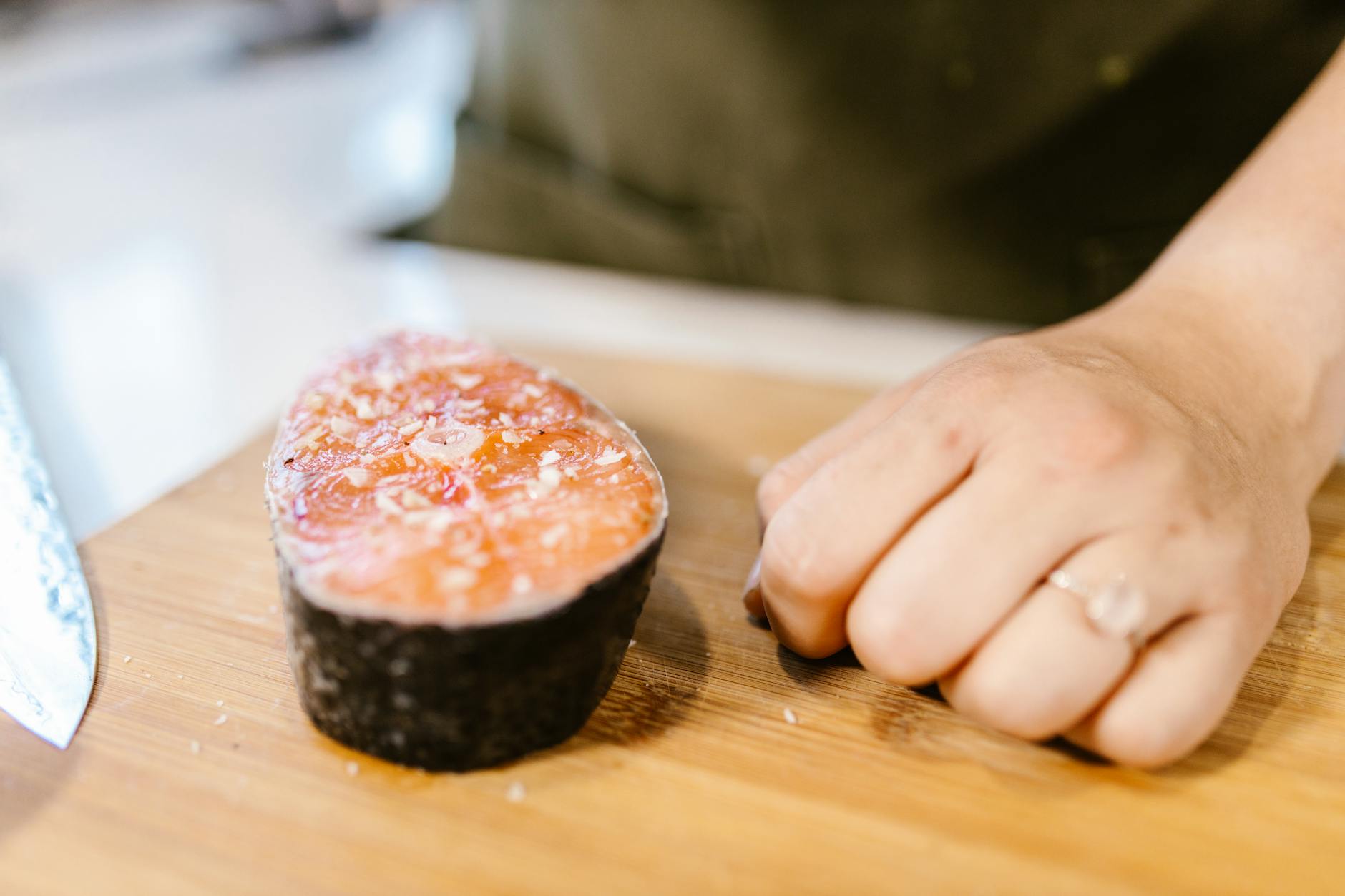 A close-up view of a fresh salmon fillet next to a hand on a cutting board.