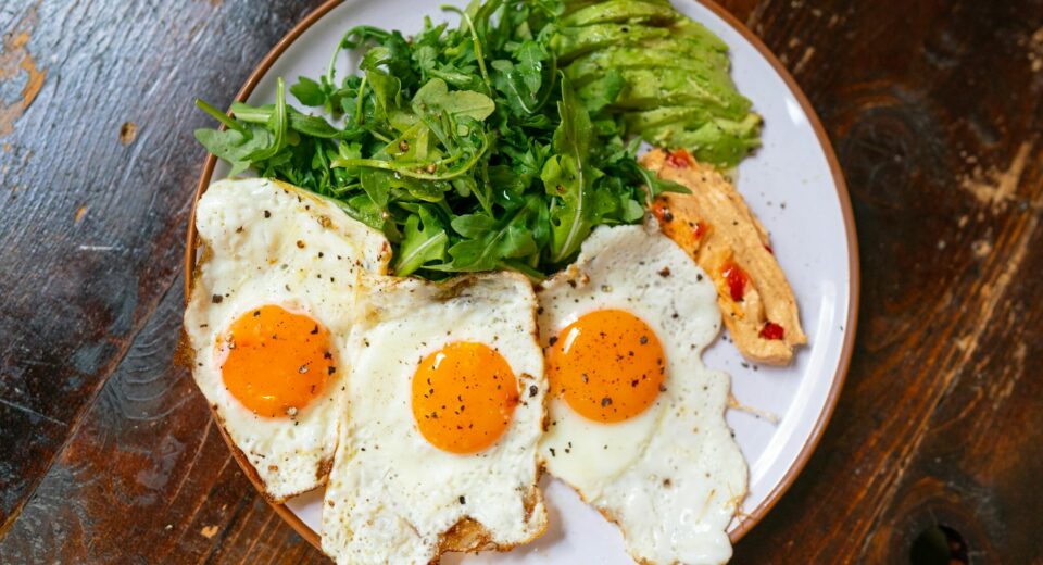Top view of a breakfast plate with eggs, arugula, avocado, and spread.