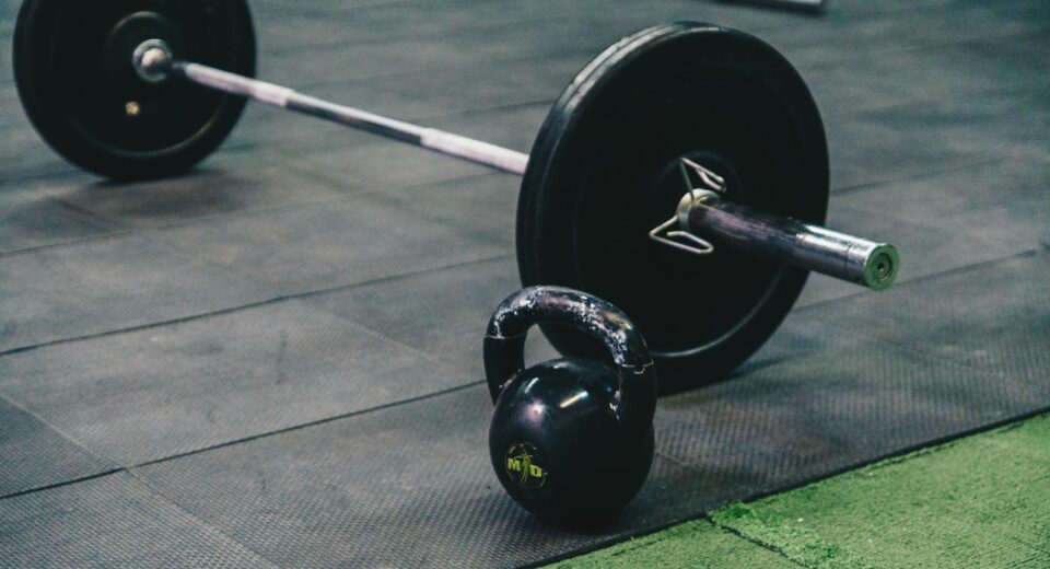 Barbell and kettlebell on gym floor, ideal for fitness and strength training themes.