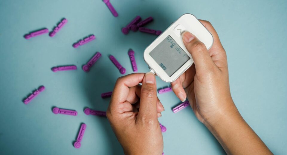 Top view of crop anonymous female diabetic measuring blood sugar with glucometer over scattered lancets