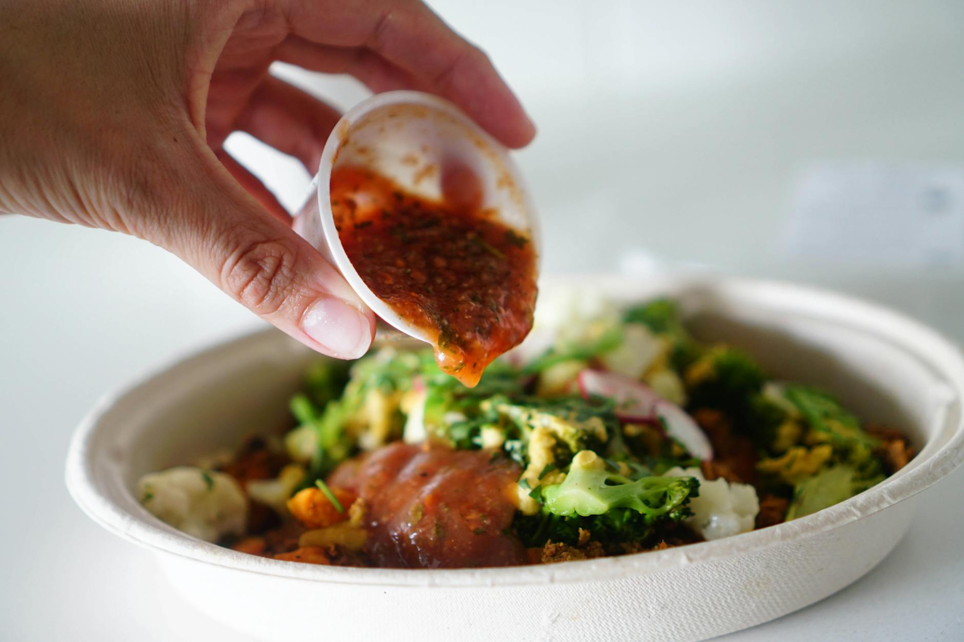 Hand pouring salsa over vegetable salad bowl, emphasizing freshness and flavor.