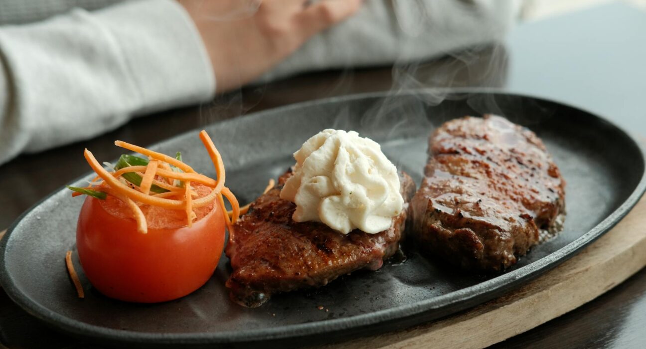 A sizzling steak served with tomato and whipped butter, perfect for food photography.