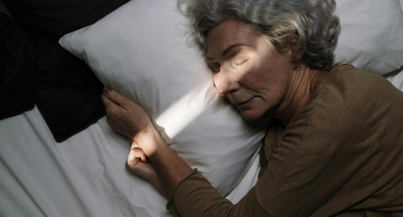 A serene moment of an elderly woman peacefully sleeping on a bed with soft lighting.