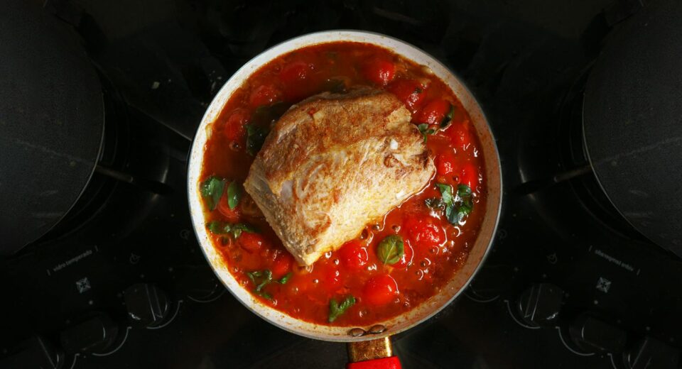 A savory roast beef cooked in rich tomato sauce with herbs, atop a stovetop.