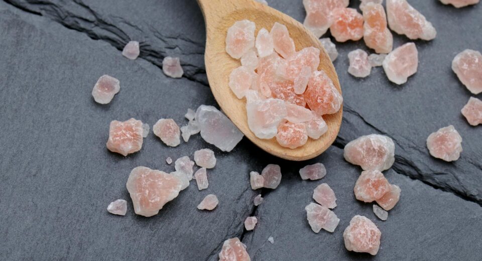 Close-up of Himalayan pink salt crystals on a wooden spoon and slate background, perfect for culinary use.